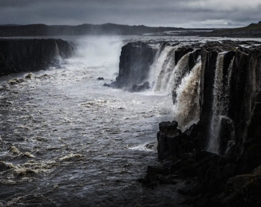 Selfoss under a dark sky, its many separate strands pouring off the basalt ledges